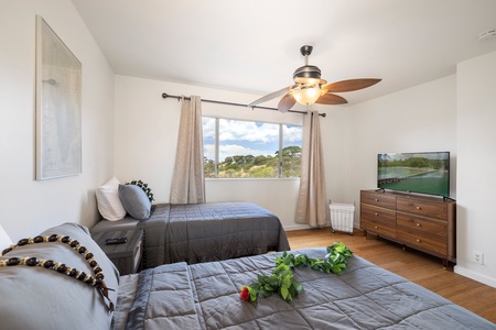 A tranquil queen bedroom features soft grey tones, hardwood floors, and windows overlooking the hillside—ideal for a guest or sitter suite.