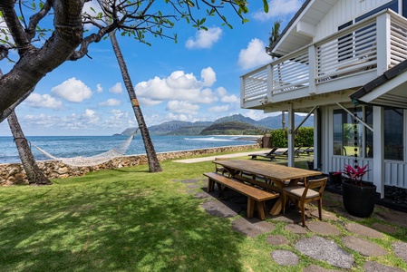 Home with oceanfront lawn, direct beach access, lounge chairs, and tropical palm trees under bright blue skies.