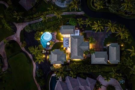 An aerial view of the property illuminated at night, showcasing the pool and lush surroundings.