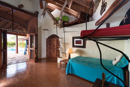 Cozy bedroom with a unique loft bed, wooden shutters, and a view of the pool.