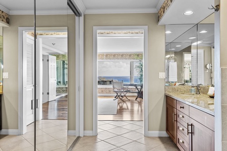 A mirrored entryway leading to a spacious bathroom with granite countertops and ocean views in the background.