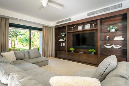 Relax in the elegant media room with a plush sectional sofa, built-in shelving, and direct access to the verdant garden.
