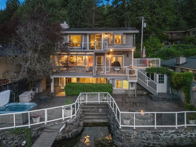 The waterfront residence lit up at dusk, tiered above its own stretch of shoreline.