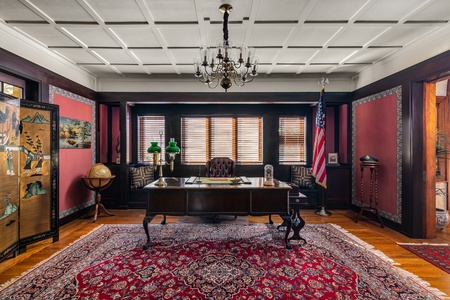 This office space has rich wood accents, a classic chandelier, and ample natural light, perfect for focused work or leisurely reading.