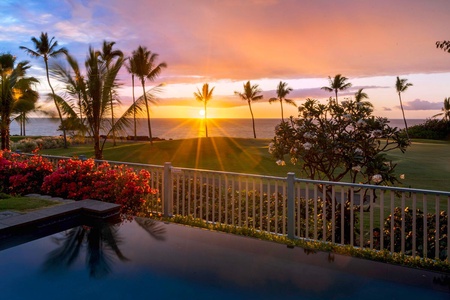 Breathtaking sunset view from a backyard pool, framed by palm trees and vibrant flowers, offering a perfect end to the day.