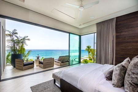 Wake up to stunning ocean views in the primary bedroom, featuring a plush bed, and floor-to-ceiling sliding doors that open to a private terrace.