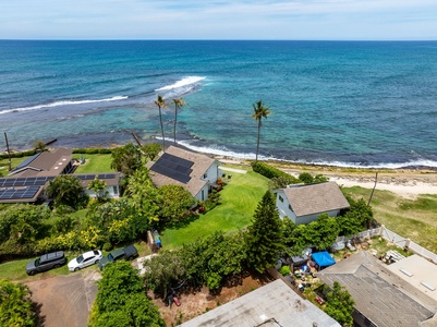 Your oceanfront vacation home with dramatic mountain backdrop and tropical palm trees creating an idyllic Hawaiian setting.