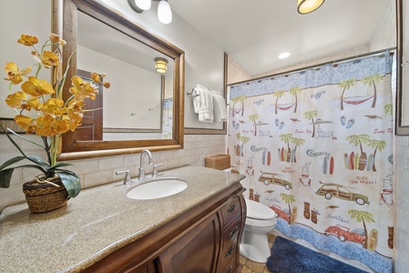 Full bathroom with granite vanity and playful island-themed shower curtain.