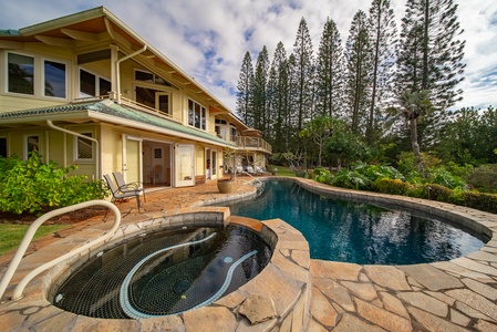 Tropical paradise featuring elegant two-story home with pristine pool, spa, and lush island landscaping under towering palm trees.