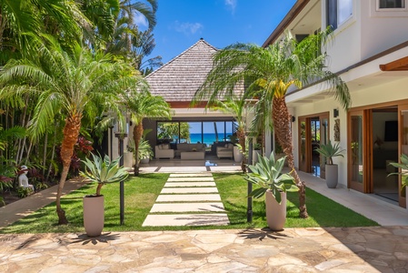 Beachfront property with lush tropical landscaping, private pool, and direct access to sandy shores, framed by swaying palms and rolling green hills.