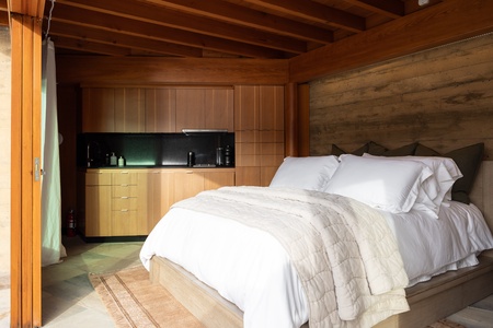 Rustic bedroom with a kitchenette, wood-paneled walls, and a cozy bed.