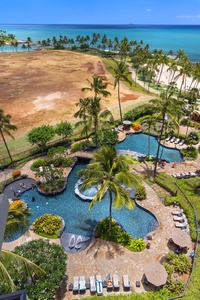 Stunning aerial view showcases the resort's lagoon-style pool surrounded by swaying palms, with pristine beach and turquoise ocean beyond.