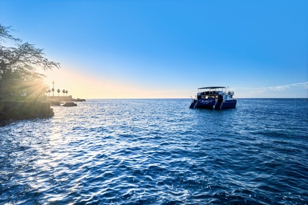 Stunning sea view with Fairwinds boat anchored in crystal-clear waters as the sun sets over the horizon.