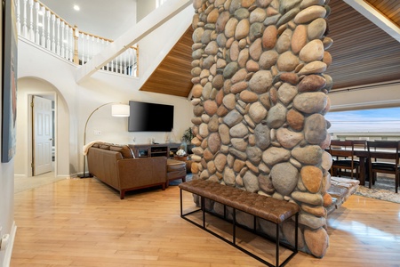 Relax in your spacious living room featuring a stunning natural stone wall, leather seating, and soaring ceilings that create an inviting atmosphere.