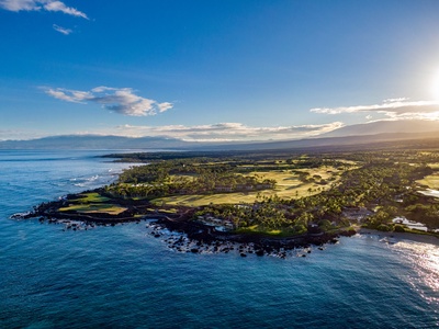 Spectacular aerial view showcasing the dramatic coastline where lush golf fairways meet volcanic shores and crystal-clear Pacific waters.