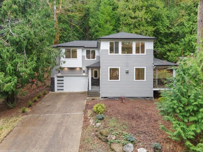 Modern two-story home nestled among towering evergreens with private driveway and landscaped front yard.