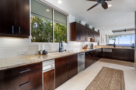 Expansive kitchen features granite countertops, rich wood cabinets, and stunning tropical views through floor-to-ceiling windows.