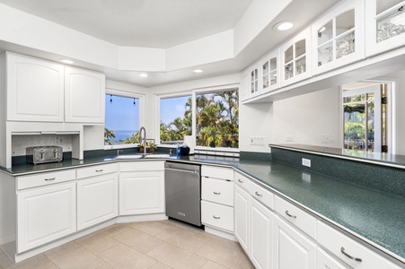 Expansive windows in this fully equipped kitchen with granite counters and white cabinetry.