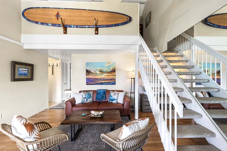 The open-concept living area features soaring vaulted ceilings and a staircase leading to the loft, creating a spacious retreat filled with natural light and island charm.