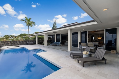 Modern villa featuring a pristine pool area with tropical palm trees and mountain views under bright blue skies.