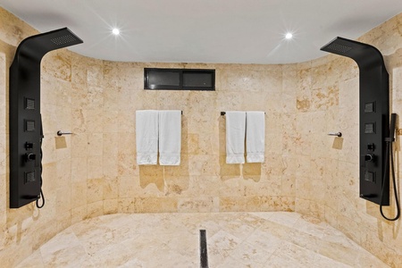 A luxurious shower room featuring dual rainfall shower heads and smooth stone tiles.