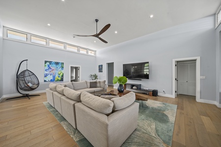 Open-concept living room with a large sectional, Smart TV, and sliding glass doors leading to the lush garden lanai.