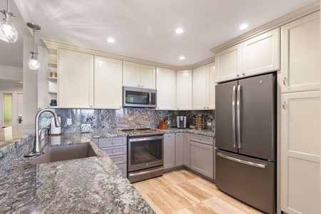 This fully remodeled kitchen boasts sleek stainless steel appliances, complemented by granite countertops and modern cabinetry, making it a perfect space for preparing meals with ease and style.