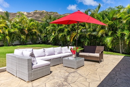 Relax on this inviting outdoor lanai, complete with plush seating and a vibrant red umbrella.