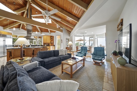 Relax in your spacious open-concept living area featuring soaring wood beam ceilings, comfortable seating, and seamless kitchen access.