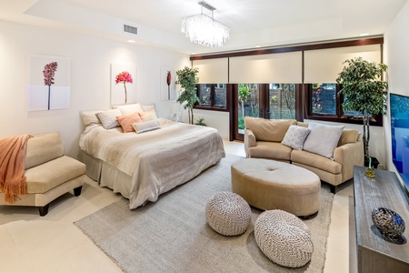 Stylish guest bedroom with seating and large windows with blinds for privacy.