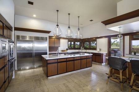 Your gourmet kitchen invites culinary adventures with gleaming stainless appliances, spacious island, and warm wood cabinetry overlooking tropical views.
