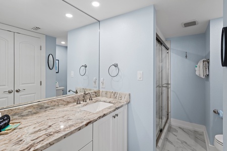 Your spacious bathroom features elegant marble countertops, soft lighting, and a modern glass-enclosed shower—perfect for refreshing after a day at the beach.