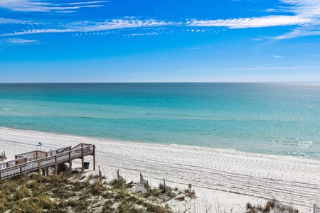 Pristine white sand beach stretches along turquoise waters under a brilliant blue sky with wispy clouds.