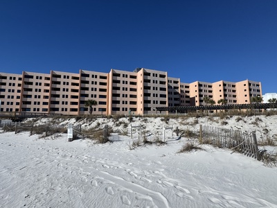 Beachfront property building sits directly on pristine white sand with clear blue skies overhead.