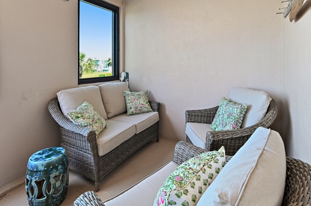 Unwind in this covered seating nook with comfortable wicker furniture and tropical-patterned pillows. The large window frames a peaceful neighborhood view, making it your perfect spot to relax with morning coffee or an afternoon read.