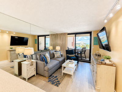 Relax in your bright, coastal-inspired living room with plush seating, charming decor, and a private balcony overlooking the scenery. Light pours through large windows, creating a warm, inviting retreat.