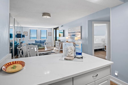 Bright coastal living opens before you, with ocean glimpses through windows framing soft blues and crisp whites. Your open kitchen flows seamlessly into the dining and living areas, perfect for relaxed beach getaway mornings.