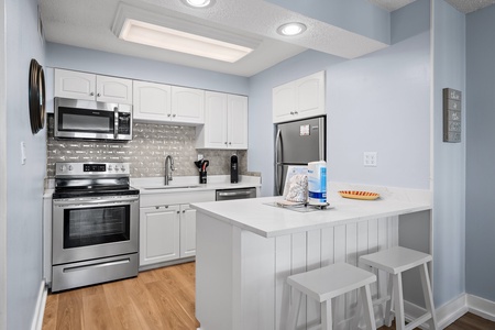 Your modern kitchen awaits with crisp white cabinetry, stainless steel appliances, and a bright breakfast bar perfect for morning coffee or meal prep.