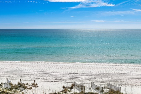 Pristine white sand beach stretches endlessly along crystal-clear turquoise waters under brilliant blue skies.