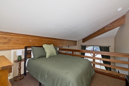 Retreat to your cozy loft bedroom, where warm wood beams and soft sage-green bedding create a peaceful haven beneath vaulted ceilings.