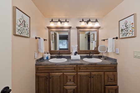 Your ensuite bathroom features elegant dual vanities with ample counter space, warm lighting, and thoughtful touches like soft towels and botanical artwork to start your day refreshed.