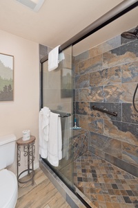Refresh in your modern bathroom with a spacious walk-in shower featuring beautiful slate-toned tilework, grab bars for safety, and fluffy white towels ready for your comfort.