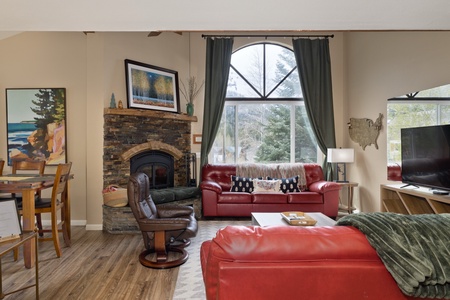 Sink into plush leather seating by your personal stone fireplace, where tall windows frame peaceful forest views and vaulted ceilings create an airy, mountain lodge ambiance.