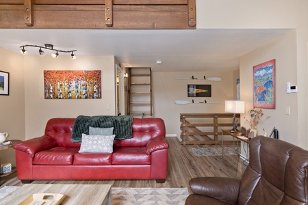 Relax in your thoughtfully designed living space, featuring cozy leather seating, vibrant artwork, and a lofted sleeping area accessed by charming ladder stairs. The open layout creates an inviting atmosphere for unwinding after exploring.