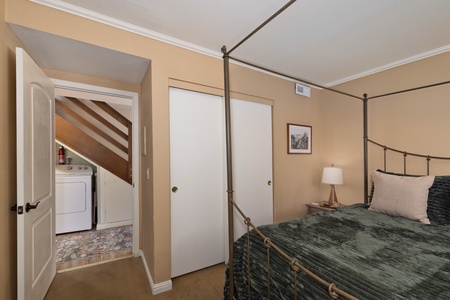 Your restful bedroom features a charming metal canopy bed with plush linens and convenient access to in-unit laundry facilities right outside your door.
