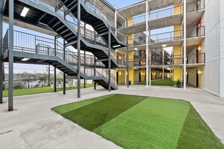 Modern apartment complex featuring multi-level concrete and steel construction with geometric green lawn spaces in the central courtyard area.