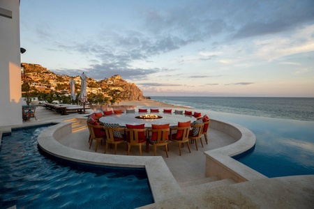 A round table with a fireplace in the middle, surrounded by chairs, sitting in the middle of a pool.