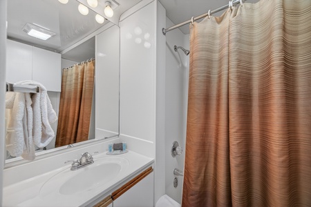 Step into your private bathroom featuring a refreshing shower-tub combo, bright vanity lighting, and plush towels ready for your arrival.