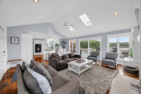 Plush seating in a bright open living room with skylight, hardwood floors, and waterfront views—ideal for relaxing or gathering with loved ones.
