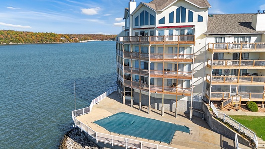 Lakefront condominium complex featuring multiple balconied units with swimming pool and autumn foliage surrounding the peaceful water.